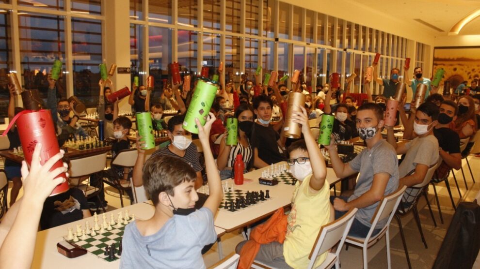 Interior do clube de xadrez com tabuleiro, peças e relógio.